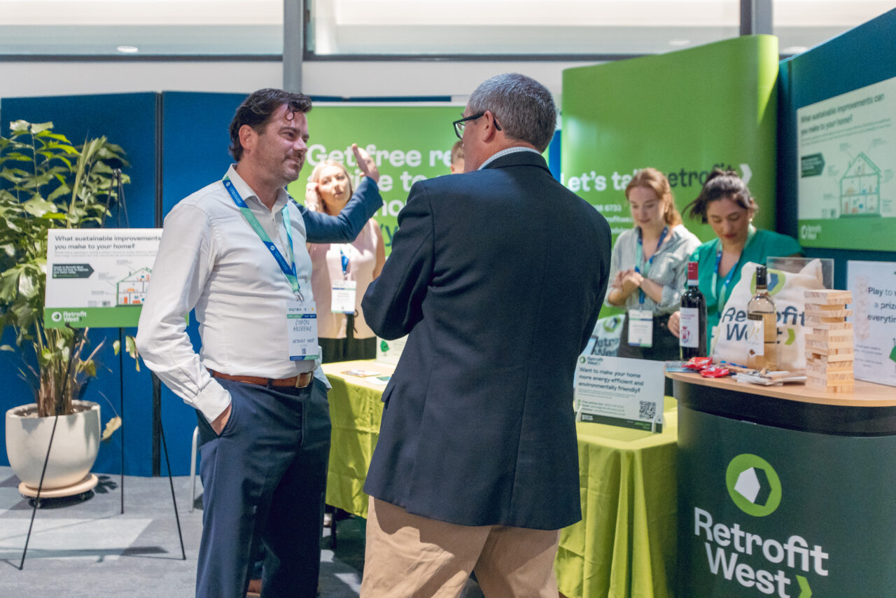 Simon Andrews, the MD at Retrofit West, talks animatedly with an individual in front of the exhibition stand. 